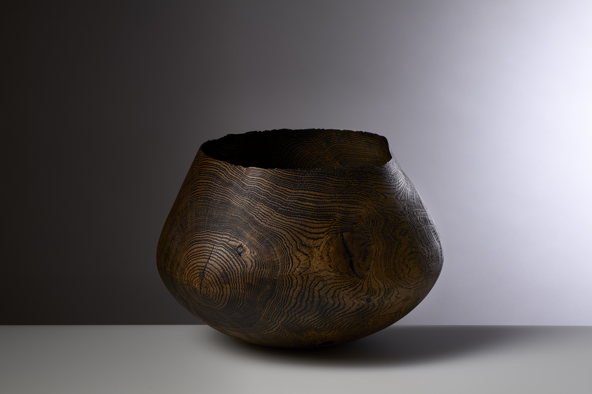 DBO 042 1 - Deutsche Manufakturenstrasse Holzschale mit ausgeprägter Maserung und unregelmäßigem Rand, auf einem hellen Tisch vor einem sanften, grauen Hintergr...