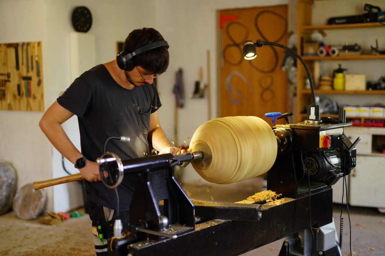 Mann arbeitet an einer Holzlathe in einer Werkstatt, Späne fliegen durch die Luft.