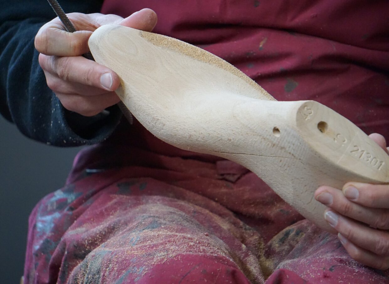 DSC05585 1 - Deutsche Manufakturenstrasse Holzform in Händen eines Handwerkers, umgeben von Holzspänen, während er an der Form arbeitet.