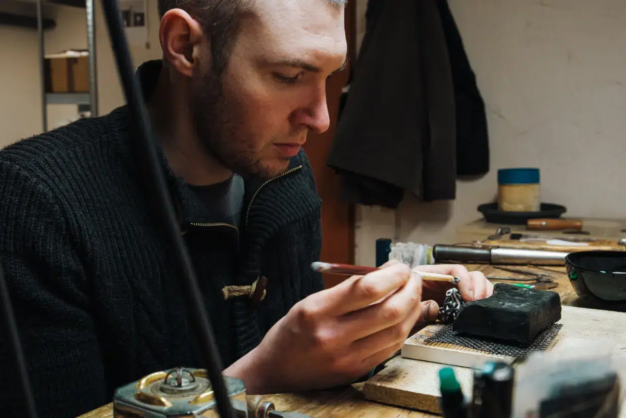 DSF4375_Werkstatt_farbig_Original - Deutsche Manufakturenstrasse Junger Mann arbeitet konzentriert in einer Werkstatt, während er ein Schmuckstück mit einem Pinsel bearbeitet.