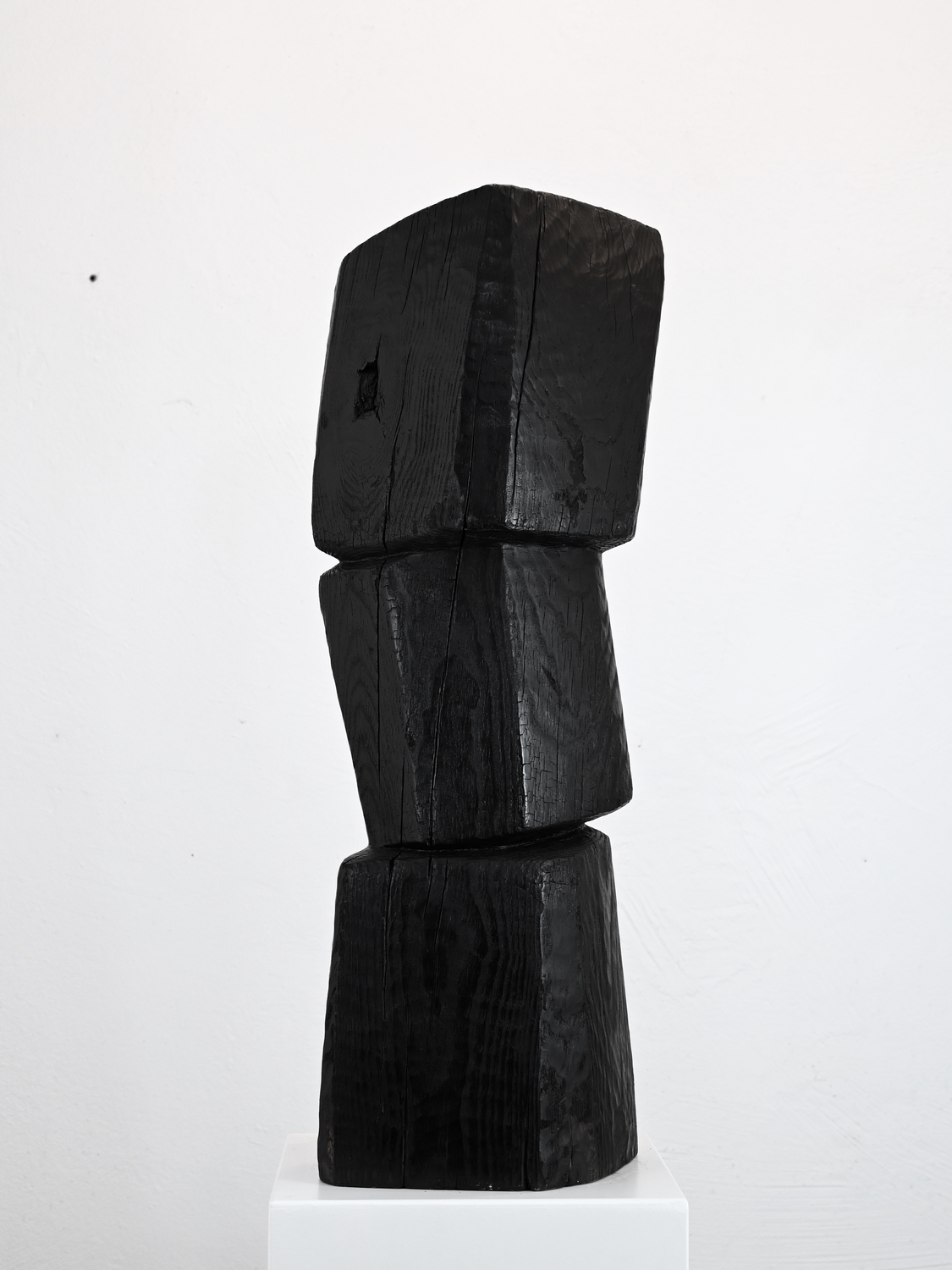 Douma_Balance 1 - Deutsche Manufakturenstrasse Dunkle Holzskulptur mit drei übereinander gestapelten, geometrischen Formen auf einem weißen Sockel.