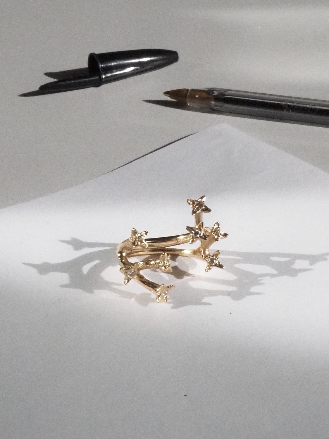 - Deutsche Manufakturenstrasse Goldring mit fünf kleinen Sternen, auf einem weißen Blatt Papier, umgeben von einem Stift und einem Bleistift.