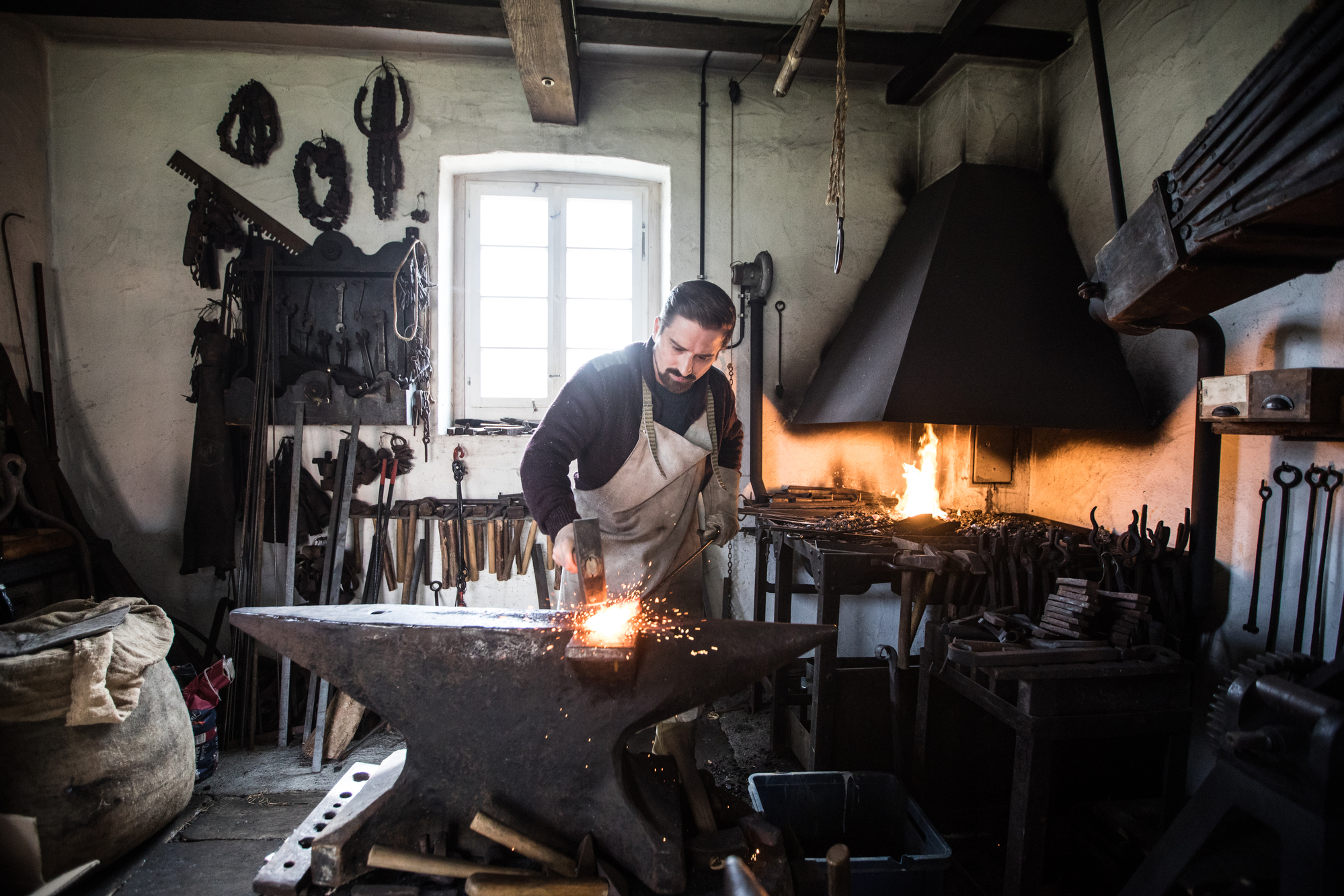 Albmesser - Deutsche Manufakturenstrasse Schmied arbeitet an einem Amboss in einer traditionellen Schmiede, Funken fliegen auf. Im Hintergrund Werkzeug und Geräte...