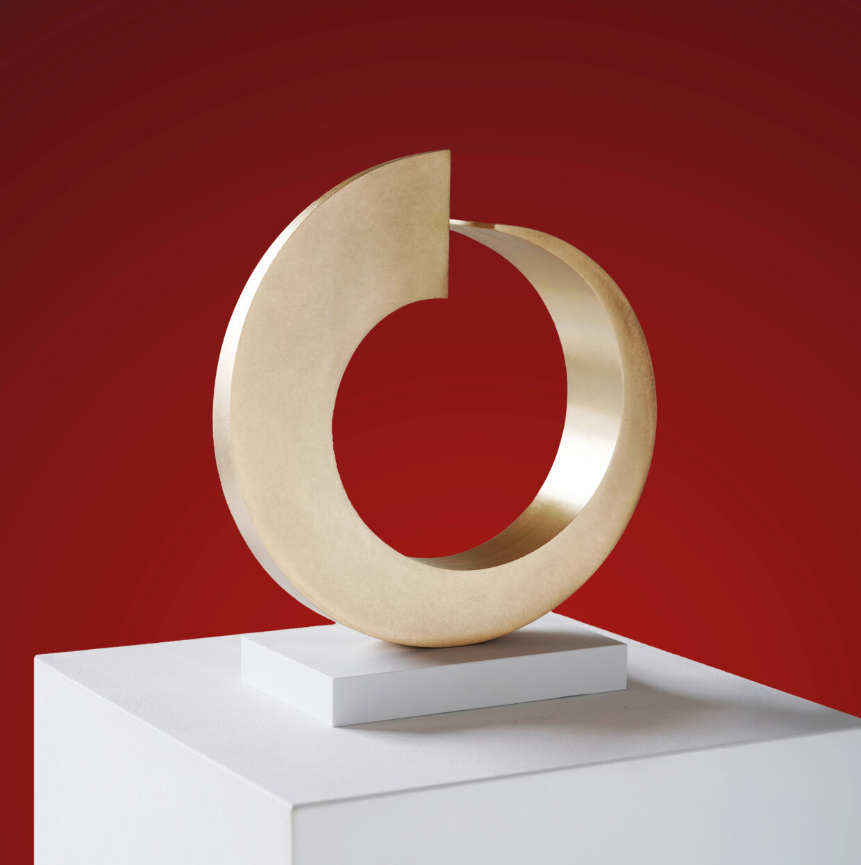 Golden Tetrahelix2025Stahl Gold285 x 26 x 8 cm 1 - Deutsche Manufakturenstrasse Goldene Tetrahelix-Skulptur auf weißem Sockel, vor rotem Hintergrund, Maße 285 x 26 x 8 cm.