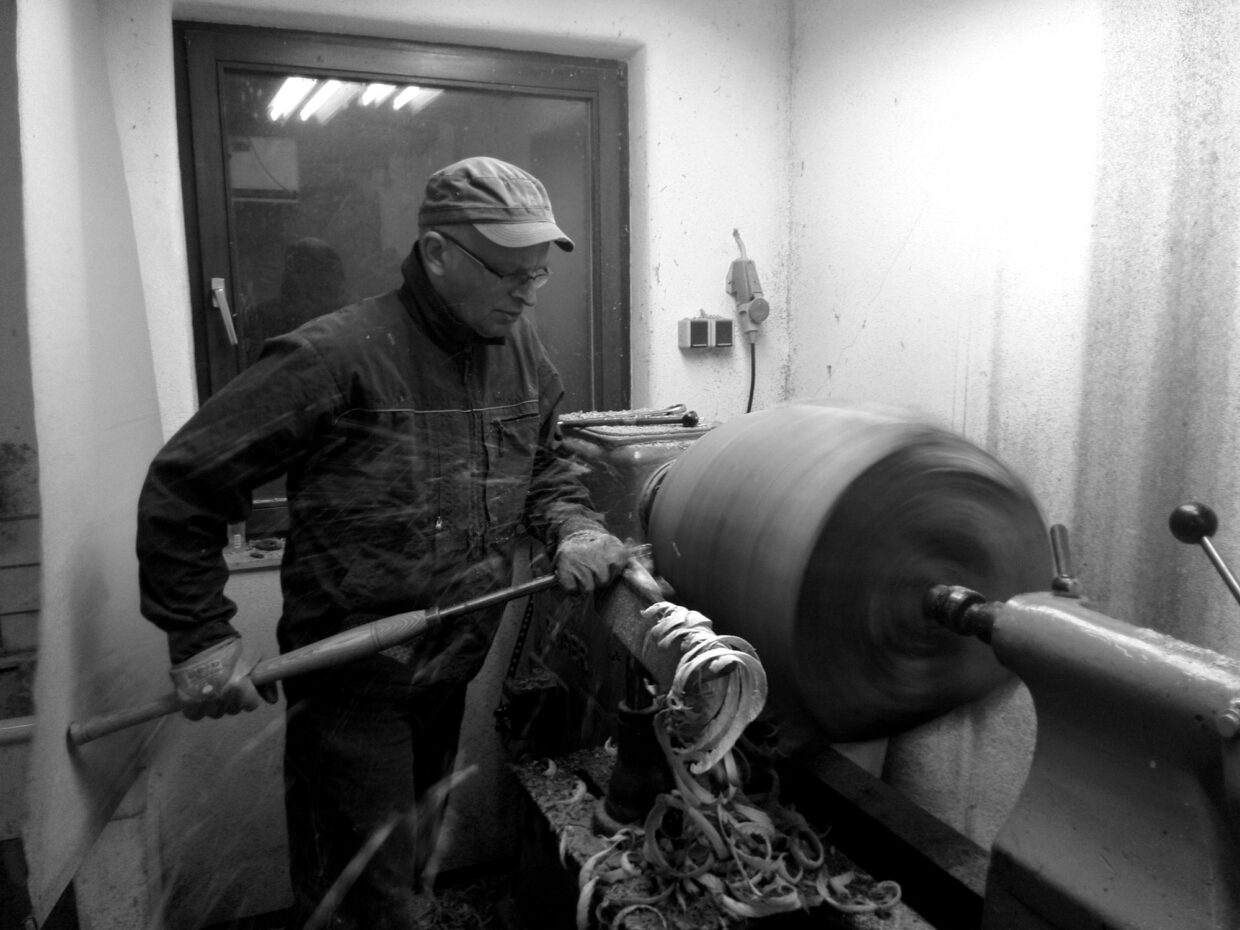 ipp - Deutsche Manufakturenstrasse Mann arbeitet an einer Drehmaschine in einer Werkstatt, Holzstück dreht sich schnell, Späne fliegen.