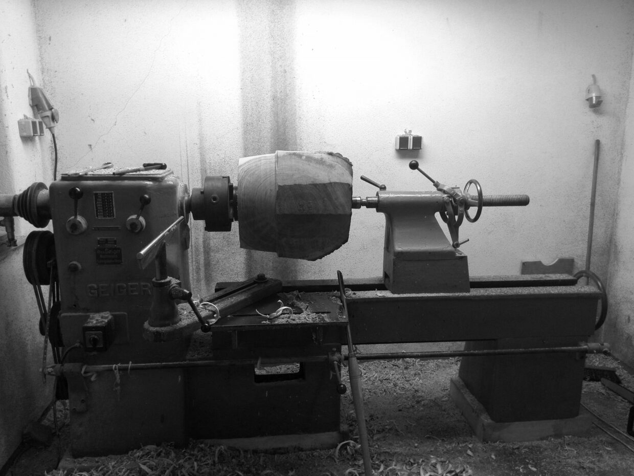 ipp - Deutsche Manufakturenstrasse Drehmaschine in einer Werkstatt, mit einem Holzstück, das bearbeitet wird, umgeben von Spänen.