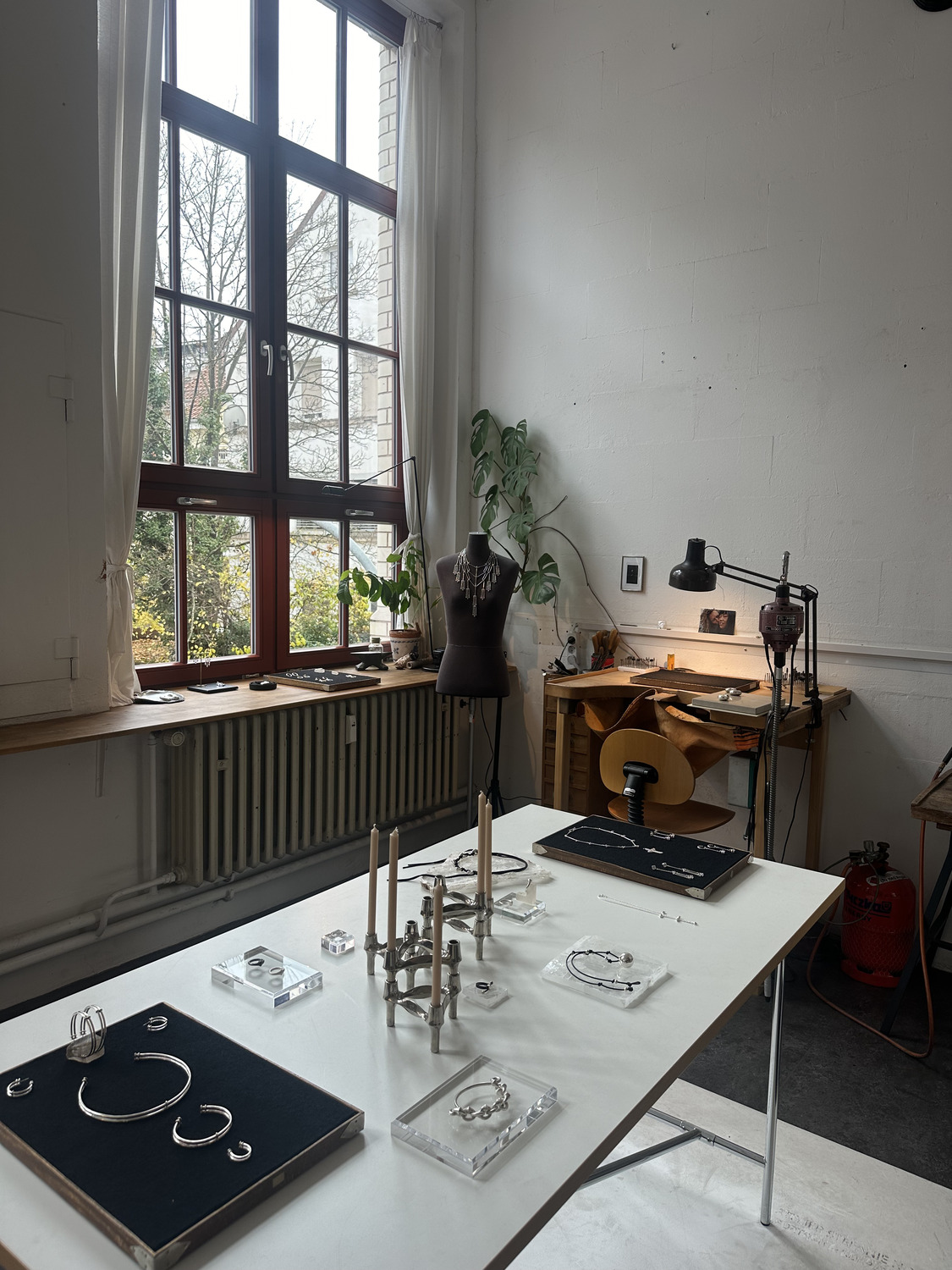 IMG_4641 1 - Deutsche Manufakturenstrasse Schmuckwerkstatt mit einem Tisch, auf dem Schmuckstücke ausgestellt sind, und einem Fenster mit Blick ins Freie.