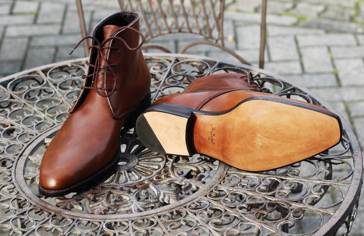 IMG_7225 2 1 - Deutsche Manufakturenstrasse Braune Lederstiefel auf einem kunstvollen Metalltisch, einer steht aufrecht, der andere liegt mit der Sohle nach oben.