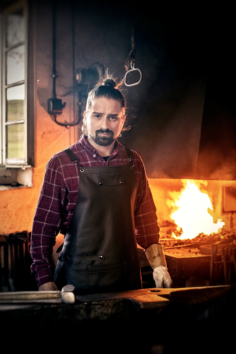 IMG_8905 1 - Deutsche Manufakturenstrasse Schmied in Arbeitskleidung steht in einer Schmiede mit Feuer im Hintergrund.