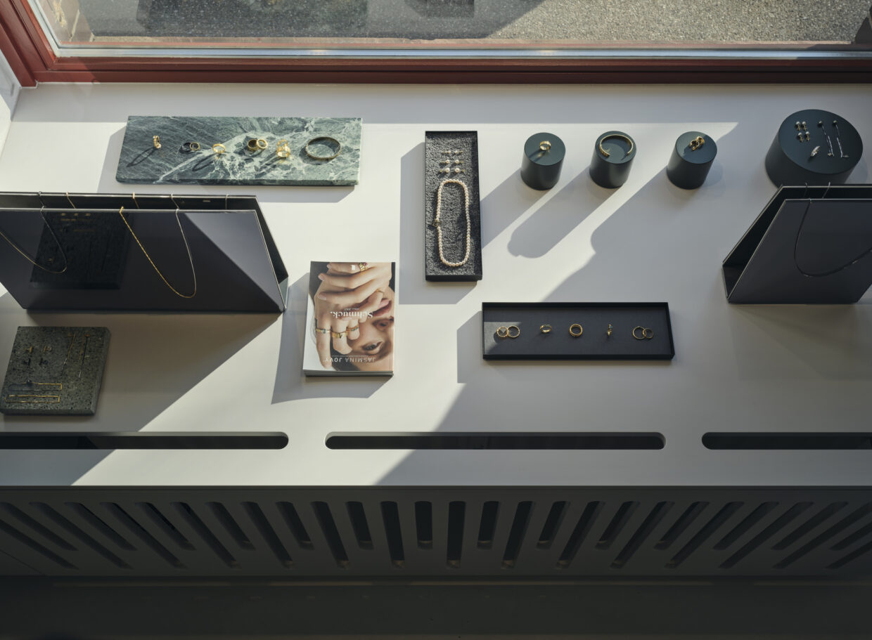 JJ_Showroom-Manufaktur_Feb2023_1668+ 1 - Deutsche Manufakturenstrasse Schmuckauslage im JJ Showroom mit verschiedenen Ringen, Armbändern und einer Broschüre auf einem hellen Tisch.