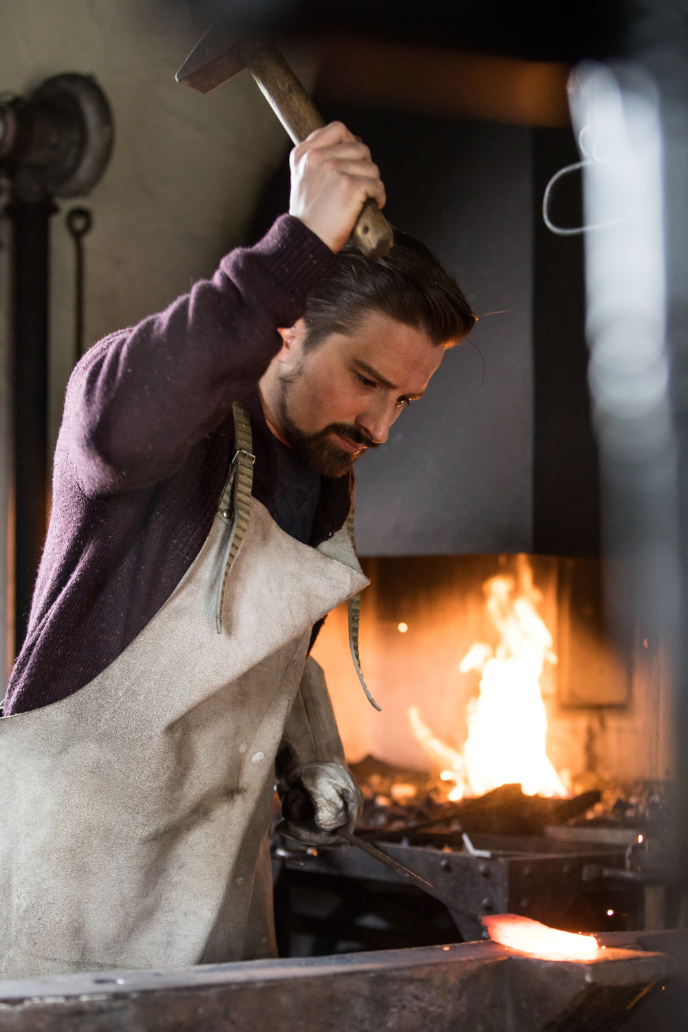 Albmesser - Deutsche Manufakturenstrasse Schmied arbeitet konzentriert an glühendem Metall in einer Werkstatt, Flammen lodern im Hintergrund.