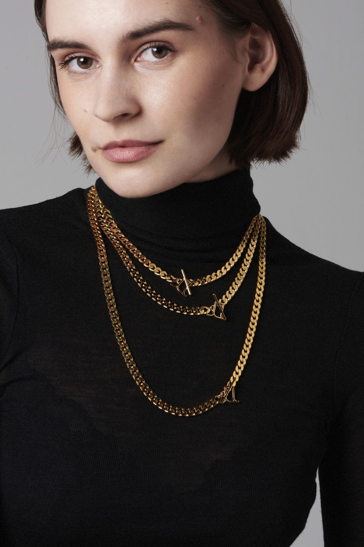 Jasmina_15882 1 - Deutsche Manufakturenstrasse Junge Frau in schwarzem Rollkragenpullover trägt mehrere goldene Ketten mit Anhängern.