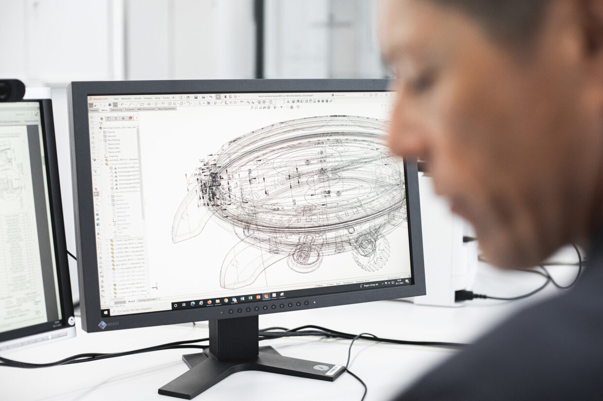 Junghans design process 1 1 - Deutsche Manufakturenstrasse Technischer Entwurf eines Junghans-Uhrenmodells auf einem Computerbildschirm, unscharfer Designer im Vordergrund.
