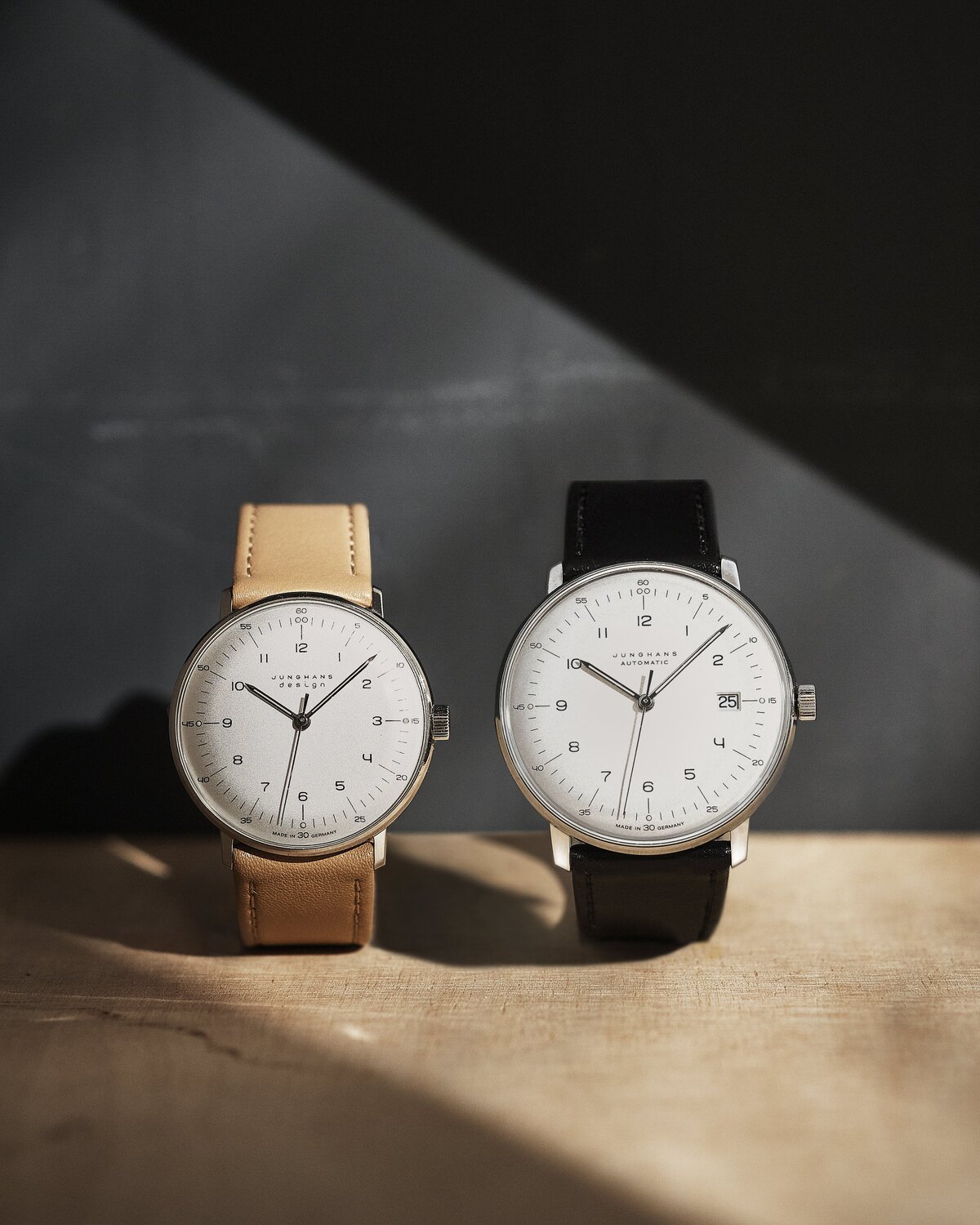 Junghans max bill_1 1 - Deutsche Manufakturenstrasse Zwei Junghans max bill Uhren mit hellen und dunklen Lederarmbändern auf einer Holzoberfläche.