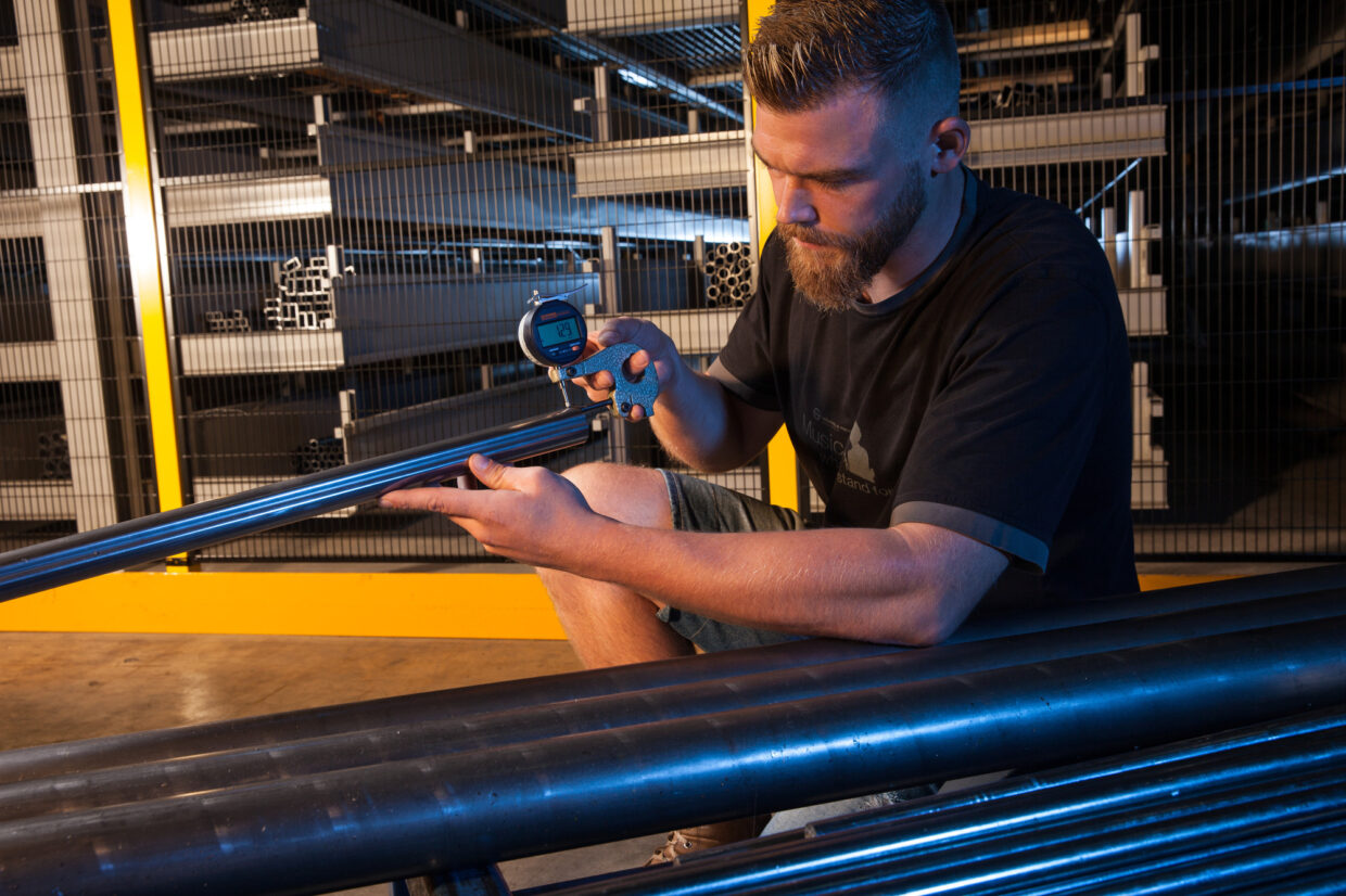 KM_004 1 - Deutsche Manufakturenstrasse Mann mit Bart misst einen Metallrohrdurchmesser mit einem Messschieber in einer Werkstatt von König + Meyer.