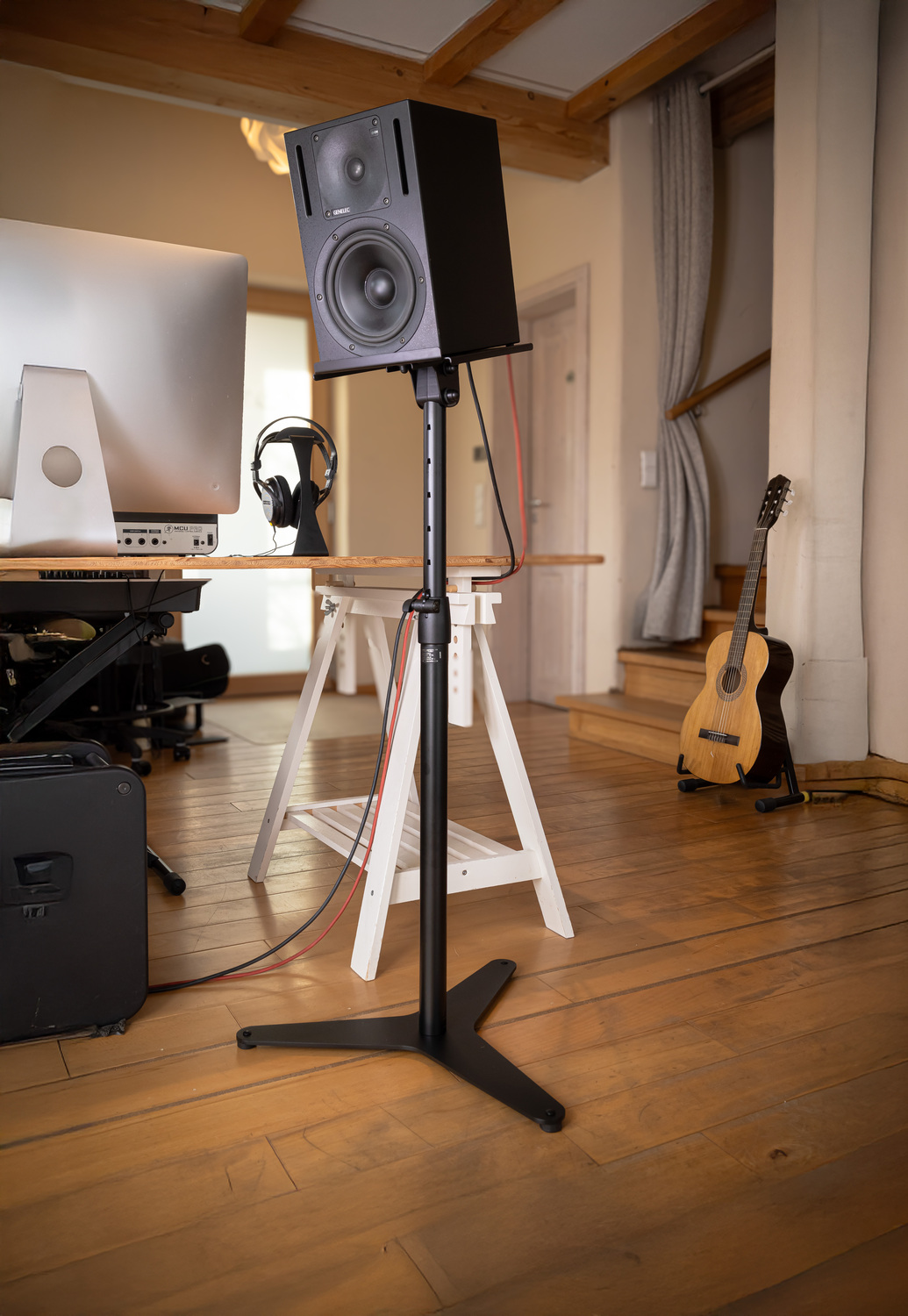 KM_006 1 - Deutsche Manufakturenstrasse Schwarzer Lautsprecher auf einem Ständer in einem Raum mit Holzfußboden, Schreibtisch und Akustikgitarre im Hintergrund.
