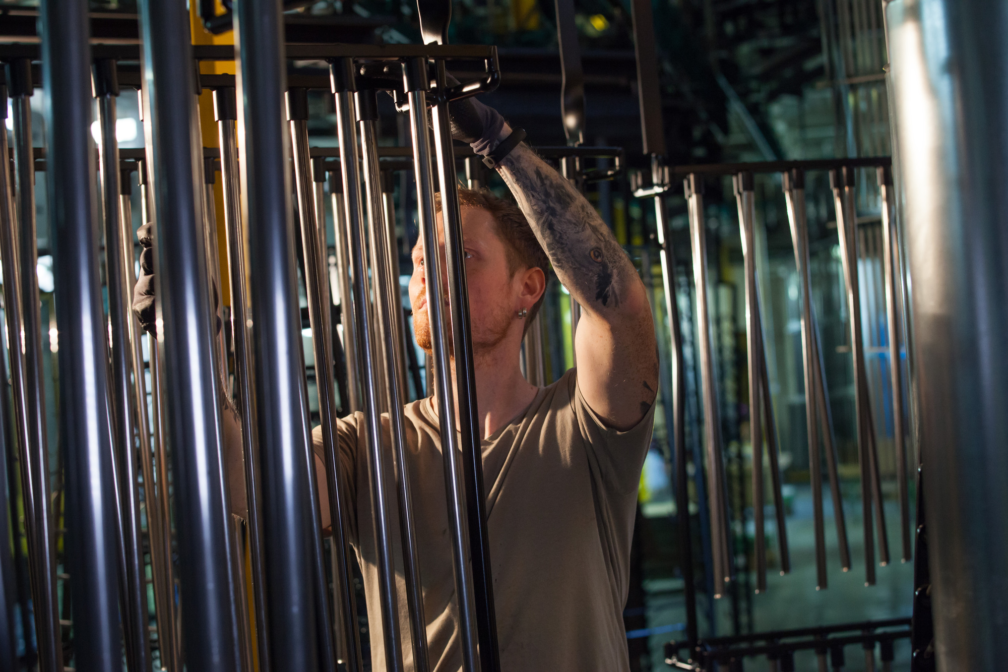 KM_009 1 - Deutsche Manufakturenstrasse Mann mit Tätowierungen montiert Metallstangen in einer Produktionsumgebung bei König + Meyer.