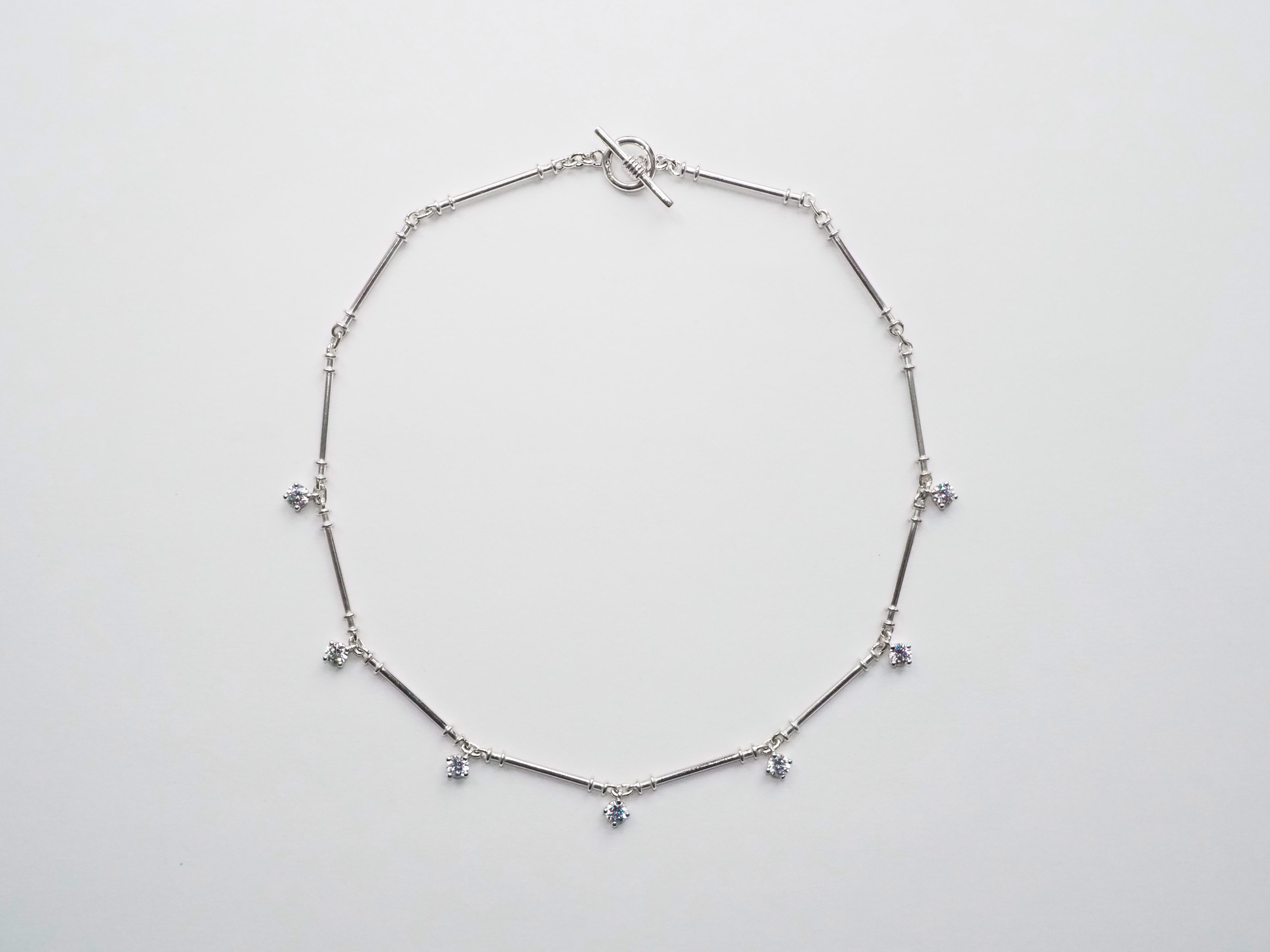 Lovers Necklace Kopie 1 - Deutsche Manufakturenstrasse Silberne Halskette mit schmalen Stäben und funkelnden Anhängern, auf hellem Hintergrund.