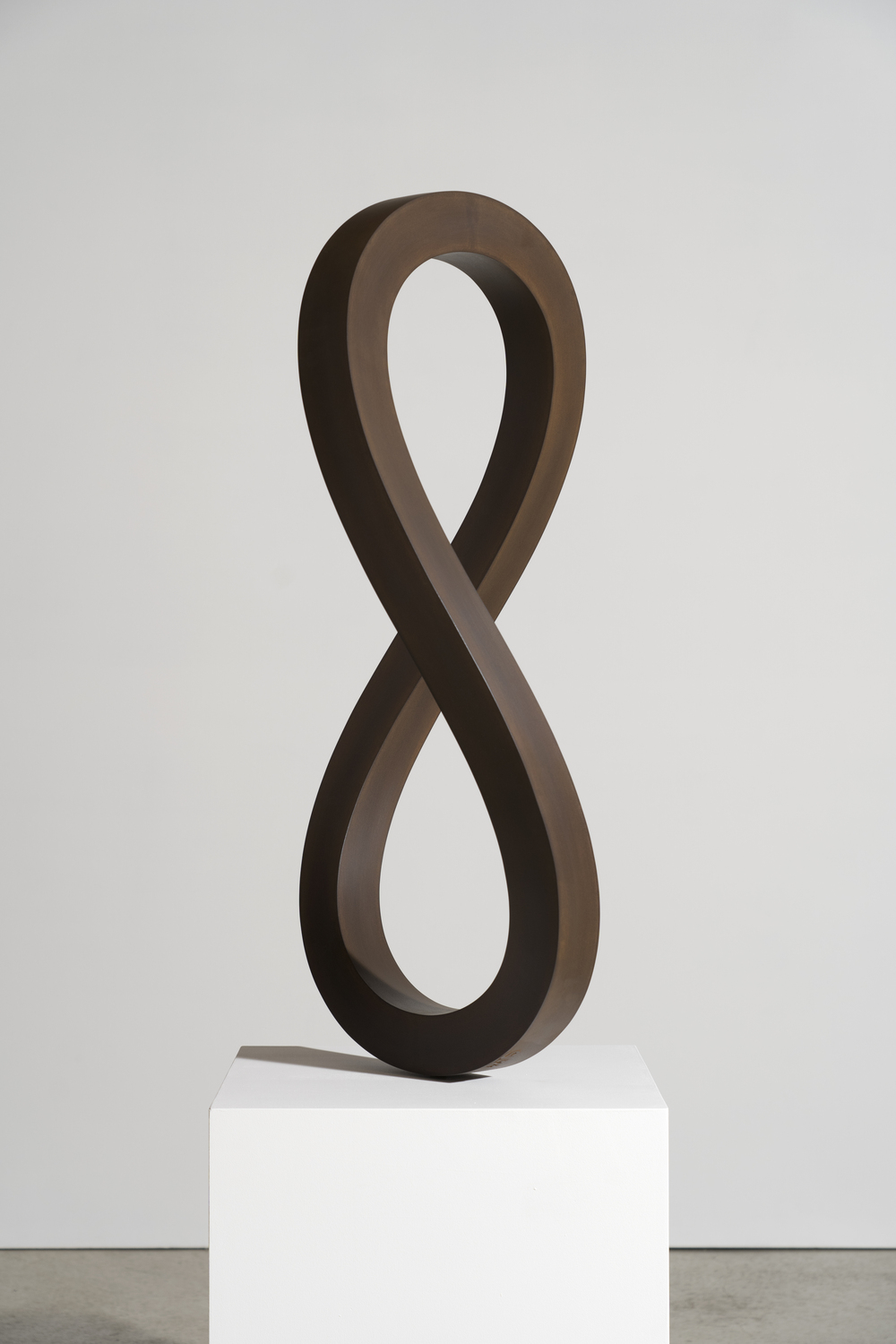 Pointer2022Corten87 x 49 x 49 cm 1 - Deutsche Manufakturenstrasse Skulptur in Form einer liegenden Acht aus Cortenstahl, auf einem weißen Sockel präsentiert.