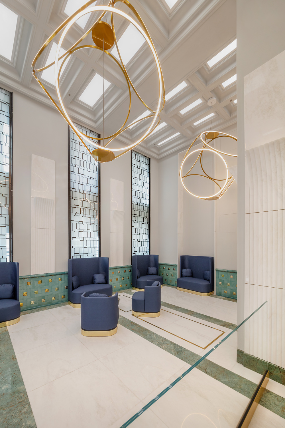 Postapalota_SATTLER-Leuchte-Unione_1750_028_Photo_Tamás_Bujnovszky - Deutsche Manufakturenstrasse Moderne Sattler-Leuchten hängen über stilvollen blauen Sitzgelegenheiten in einem eleganten Raum mit Marmor- und Glasele...