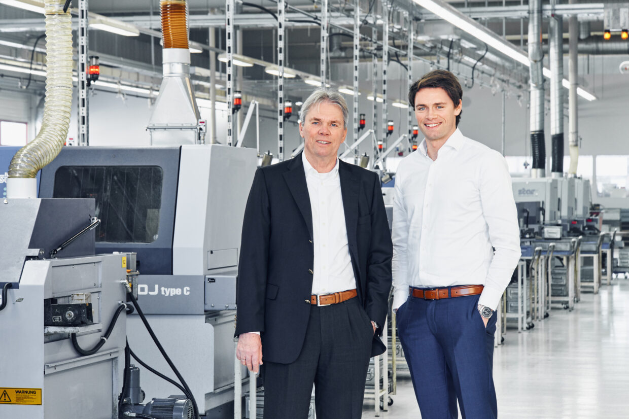 Rolf and Dominik Hermle 1 - Deutsche Manufakturenstrasse Rolf und Dominik Hermle stehen in einer modernen Produktionshalle neben Maschinen.