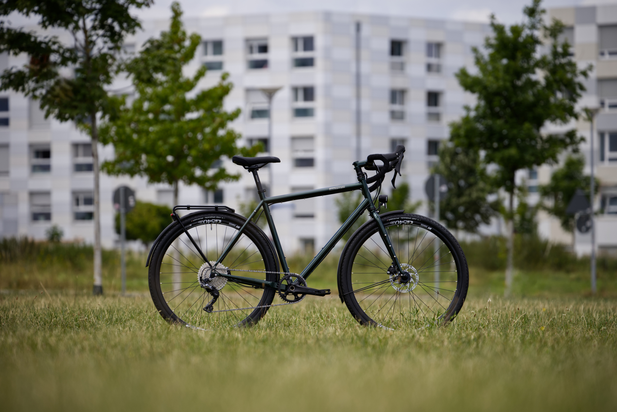 Tout Terrain Nolita GT 6 1 - Deutsche Manufakturenstrasse Grünes Tout Terrain Nolita GT 6 Fahrrad steht auf einer Wiese vor modernen Wohngebäuden.