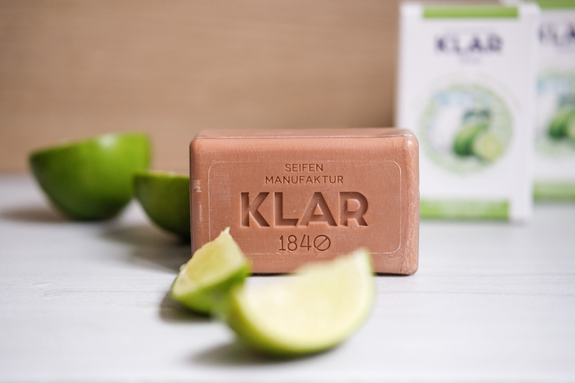WEB584153631-20240207_up_klar_116 - Deutsche Manufakturenstrasse Seife der Marke Klar mit der Aufschrift „Klar 1840“, umgeben von Limettenscheiben auf einem hellen Untergrund.