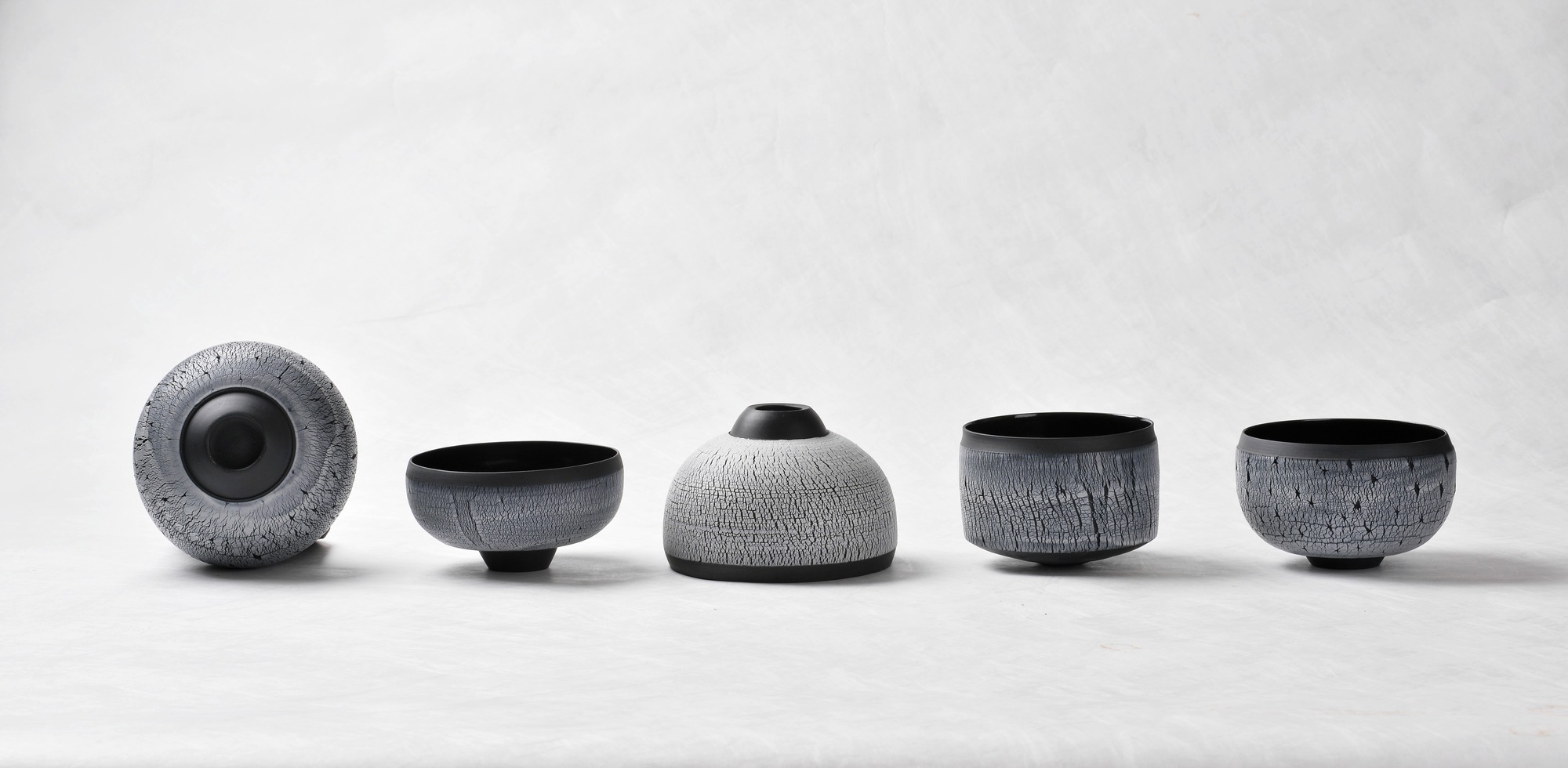 black beautys 1 - Deutsche Manufakturenstrasse Fünf keramische Schalen in verschiedenen Formen und Größen, mit schwarzer und grauer Textur, auf einem hellen Hintergrund.
