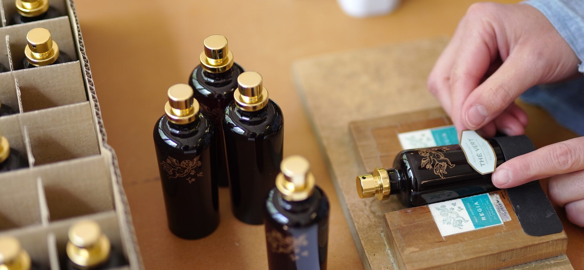 etikettieren 33 - Deutsche Manufakturenstrasse Schwarze Flaschen mit goldenen Verschlüssen werden etikettiert, während eine Hand ein Etikett aufbringt.