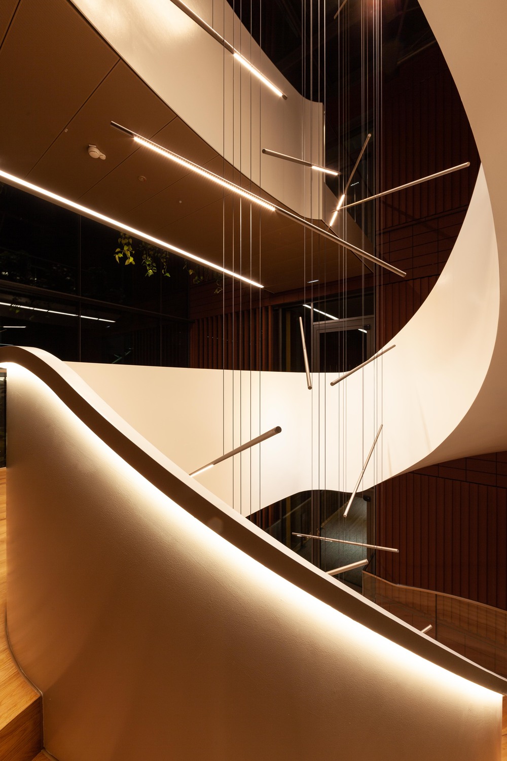 he_0078-72_Bildnachweis_Palito-SATTLER_Vector-Regensburg_FAKTORLicht 1 - Deutsche Manufakturenstrasse Moderne Treppe mit geschwungener Form, beleuchtet von hängenden Lichtleisten in einem eleganten Innenraum.