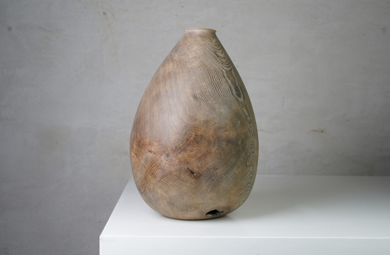 height_43cm_oak 1 - Deutsche Manufakturenstrasse Eierförmige Vase aus Eichenholz mit feiner Maserung, auf einem weißen Tisch vor grauem Hintergrund.
