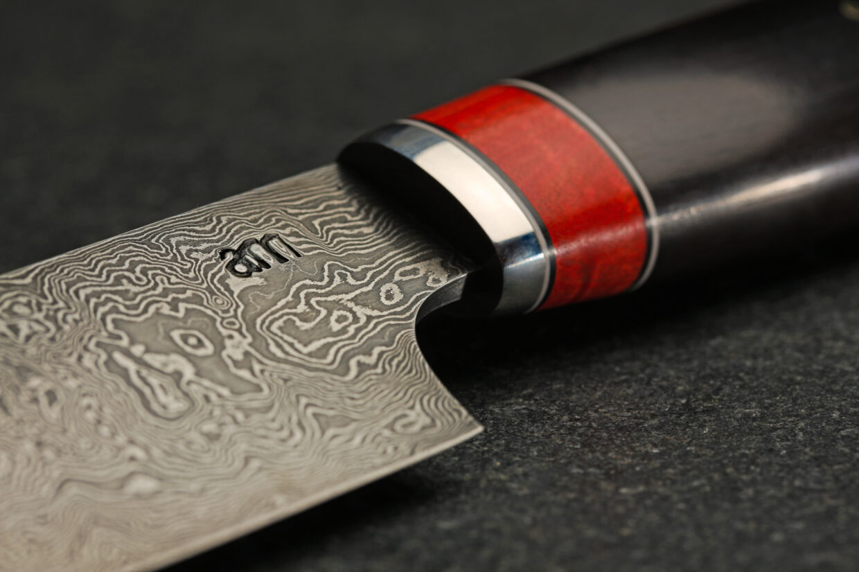 image3 1 - Deutsche Manufakturenstrasse Detailaufnahme eines Damastmessers mit einem kunstvollen Griff aus Holz und Metall, auf einer dunklen Oberfläche.