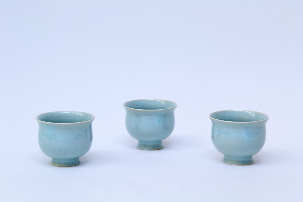 w5 1 - Deutsche Manufakturenstrasse Drei hellblaue Keramiktassen mit runder Form und breitem Fuß auf einem hellen Hintergrund.