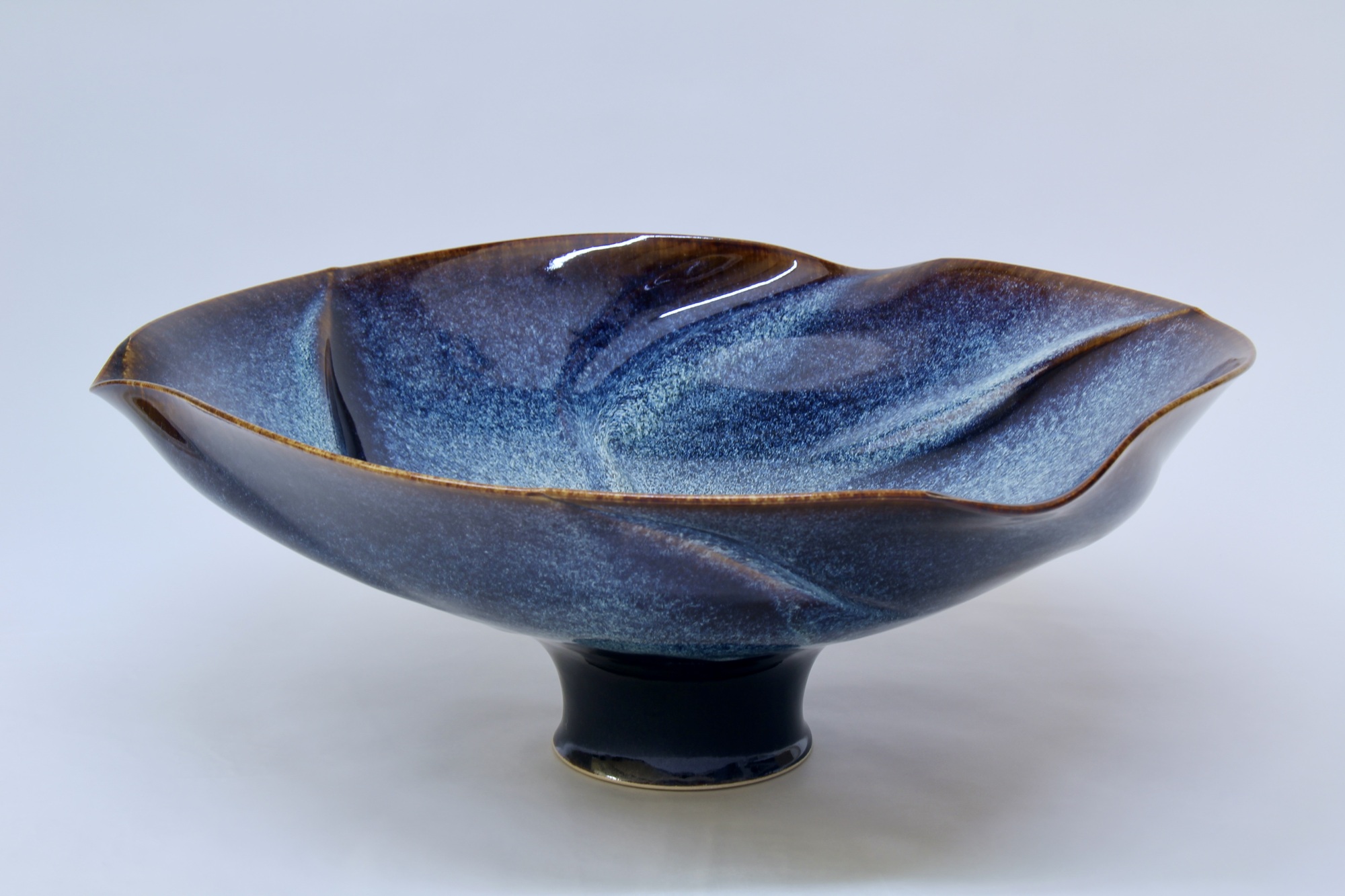 w9 1 - Deutsche Manufakturenstrasse Schale mit wellenförmigem Rand in Blau- und Brauntönen, glänzende Oberfläche, auf einem kurzen Sockel.
