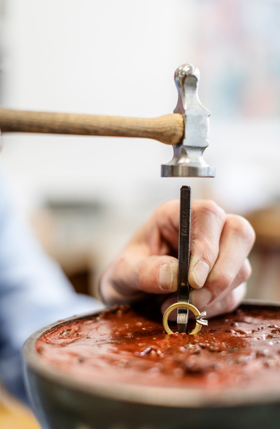 _J4A1349 - Deutsche Manufakturenstrasse Hand eines Handwerkers, der mit einem Hammer und einem Werkzeug einen Ring in eine rote Masse drückt.